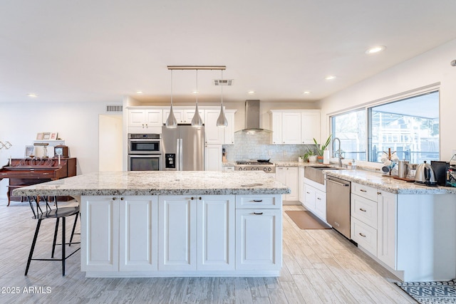 kitchen with stainless steel appliances, visible vents, a sink, and wall chimney range hood