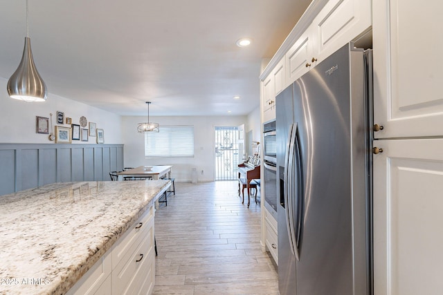 kitchen with light stone counters, light wood-style flooring, stainless steel appliances, white cabinetry, and decorative light fixtures