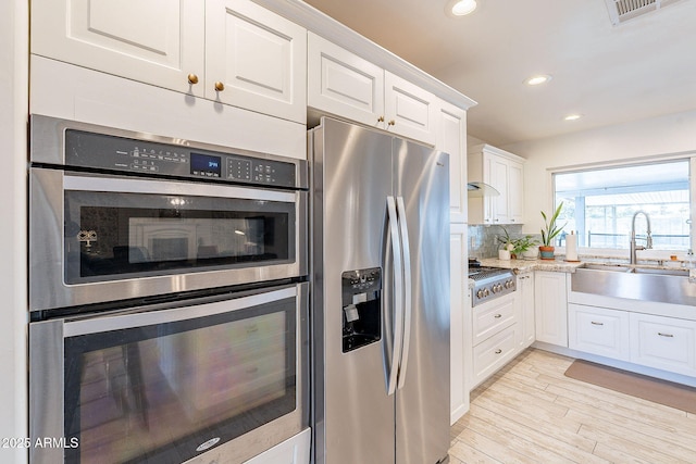 kitchen with visible vents, white cabinets, a sink, stainless steel appliances, and backsplash