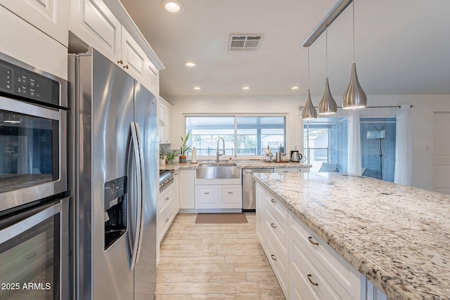 kitchen with stainless steel appliances, light stone counters, visible vents, and white cabinetry