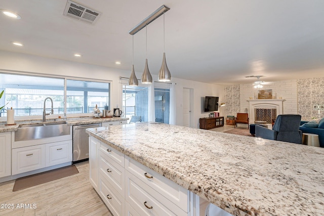 kitchen featuring a fireplace, a sink, visible vents, white cabinets, and stainless steel dishwasher