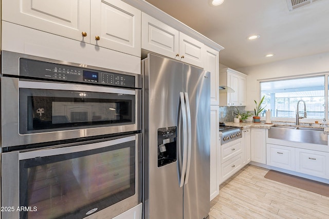 kitchen featuring decorative backsplash, white cabinets, appliances with stainless steel finishes, light wood-style floors, and a sink