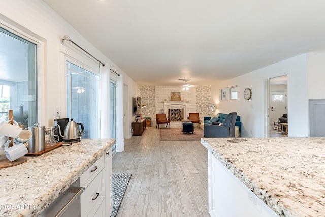 kitchen with light stone counters, light wood finished floors, a brick fireplace, white cabinets, and ceiling fan