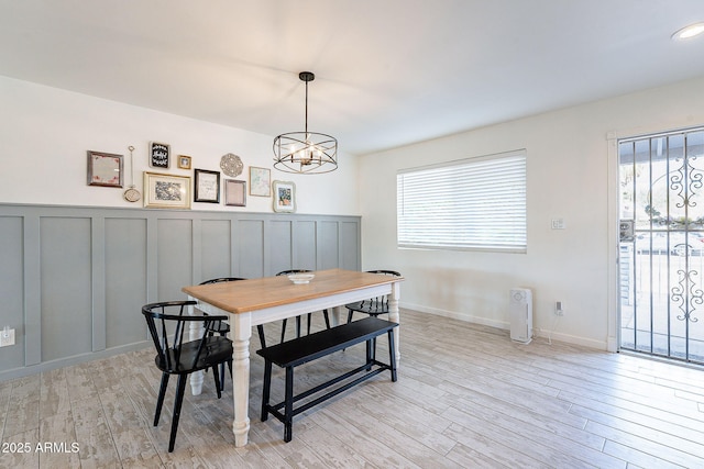 dining room featuring light wood-style floors, a wealth of natural light, a chandelier, and a decorative wall