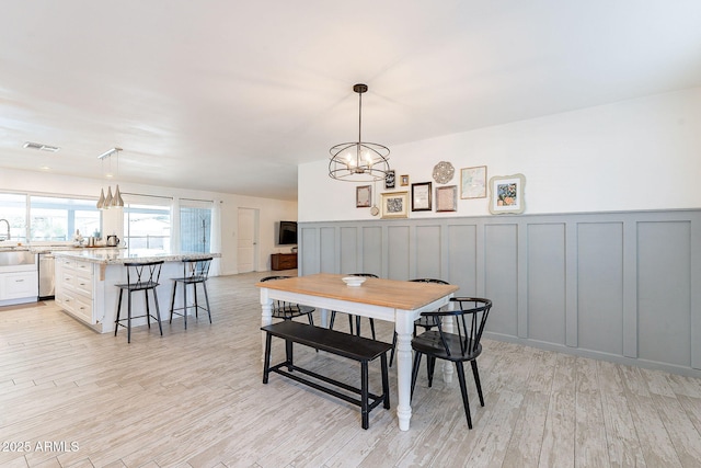 dining area with a chandelier, visible vents, a decorative wall, and light wood finished floors