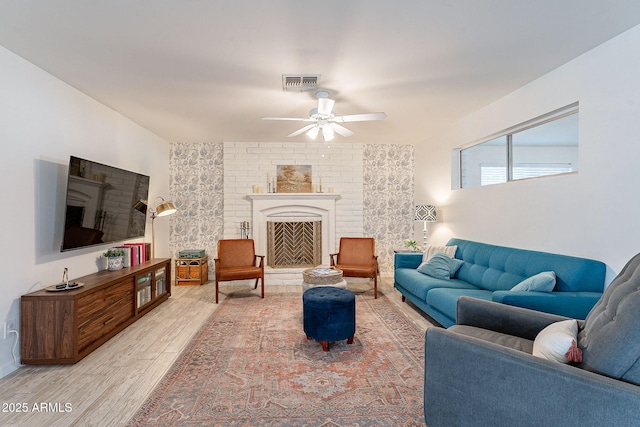 living area with ceiling fan, visible vents, a fireplace with raised hearth, and wood finished floors