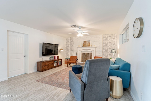 living room with a fireplace with raised hearth, wood finished floors, visible vents, baseboards, and a ceiling fan