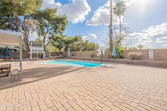 view of swimming pool featuring a patio, a trampoline, and a fenced backyard