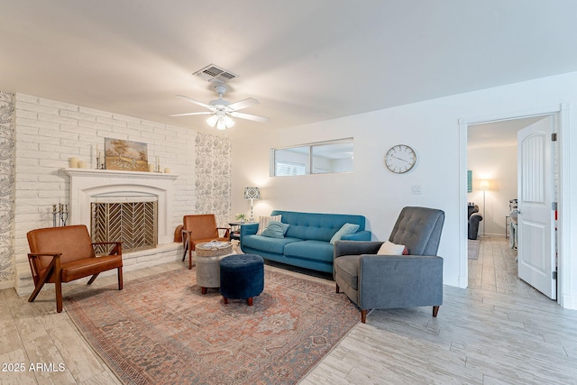 living area with visible vents, a fireplace with raised hearth, light wood finished floors, and ceiling fan