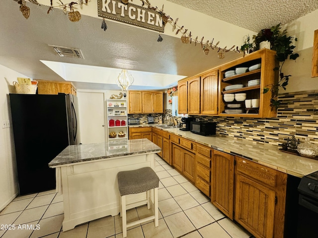 kitchen featuring a textured ceiling, a center island, a kitchen bar, stainless steel fridge, and light tile patterned floors