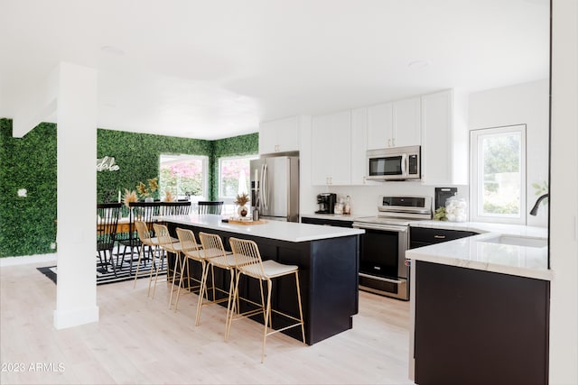 kitchen featuring sink, a breakfast bar area, white cabinetry, stainless steel appliances, and a kitchen island