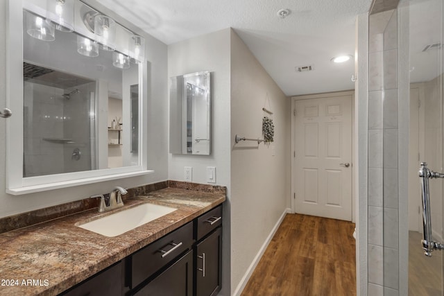 bathroom featuring visible vents, baseboards, tiled shower, wood finished floors, and vanity