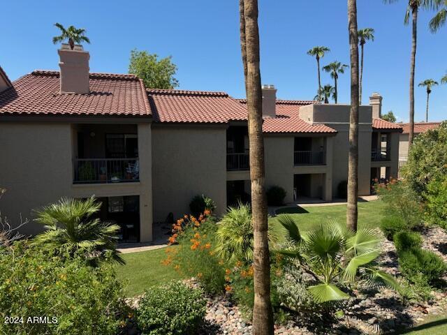 rear view of property featuring a tiled roof, a yard, a chimney, and stucco siding