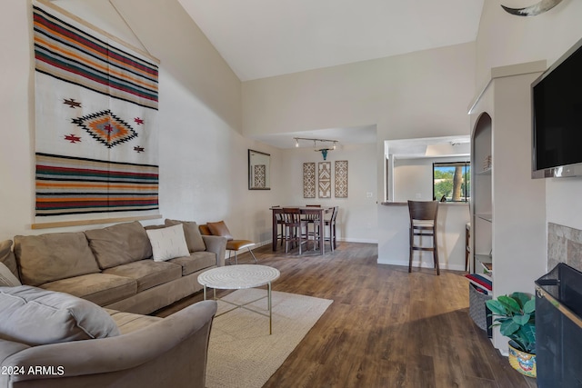 living room with wood finished floors, a fireplace, rail lighting, baseboards, and vaulted ceiling