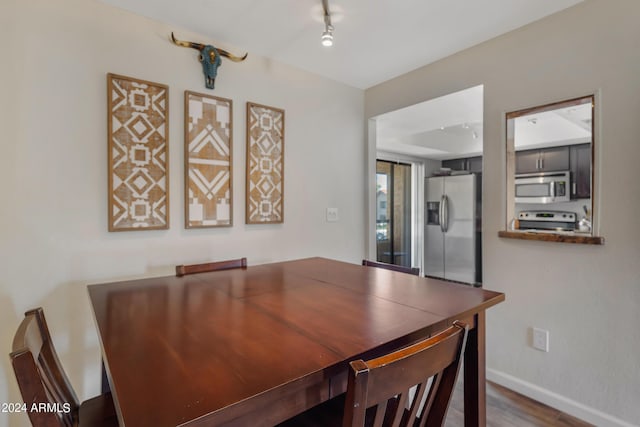 dining space featuring baseboards, wood finished floors, and rail lighting