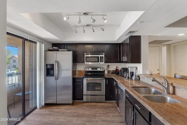 kitchen with dark brown cabinets, light stone counters, light wood-style floors, stainless steel appliances, and a sink