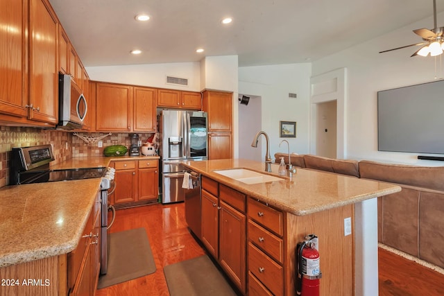 kitchen with sink, a kitchen island with sink, stainless steel appliances, vaulted ceiling, and decorative backsplash