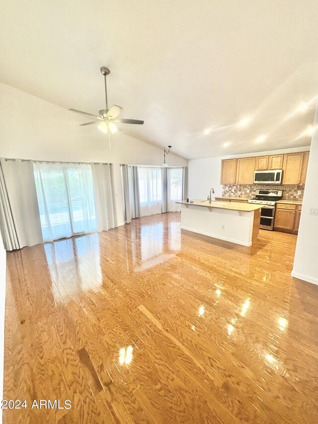 kitchen featuring stainless steel appliances, wood-type flooring, lofted ceiling, a kitchen island with sink, and sink