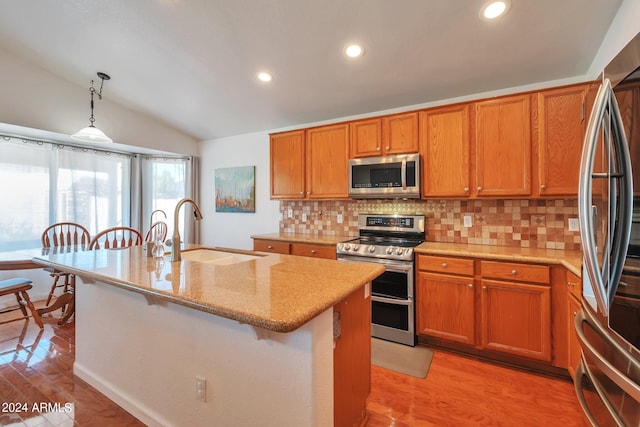 kitchen with vaulted ceiling, stainless steel appliances, light hardwood / wood-style flooring, a kitchen island with sink, and sink