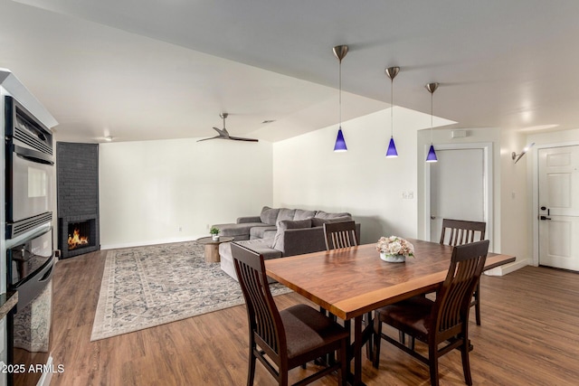 dining area featuring baseboards, a ceiling fan, lofted ceiling, wood finished floors, and a brick fireplace