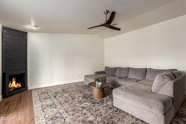 living room featuring a large fireplace, baseboards, lofted ceiling, ceiling fan, and wood finished floors