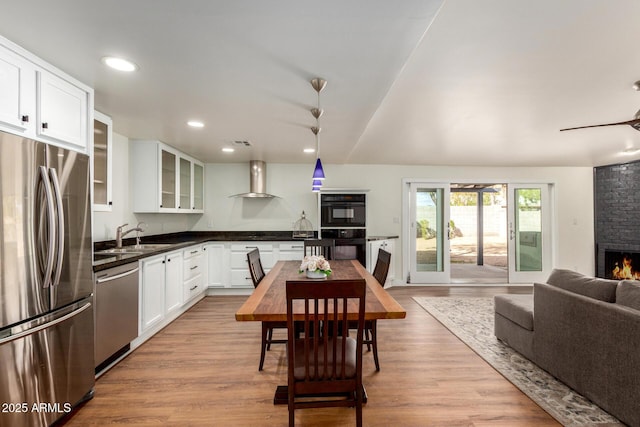 kitchen featuring light wood finished floors, appliances with stainless steel finishes, a brick fireplace, and wall chimney range hood