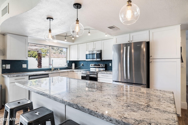 kitchen featuring pendant lighting, white cabinetry, stainless steel appliances, light stone counters, and tasteful backsplash