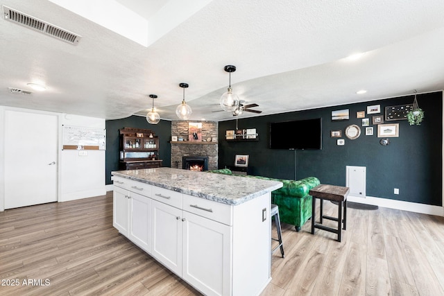 kitchen with a fireplace, white cabinets, a center island, light hardwood / wood-style floors, and light stone countertops