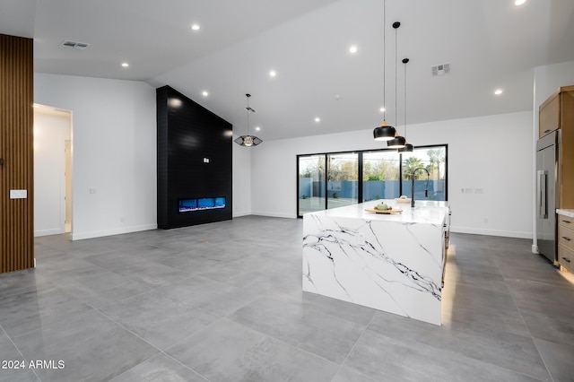 kitchen featuring light stone countertops, a large island with sink, stainless steel built in fridge, a fireplace, and hanging light fixtures