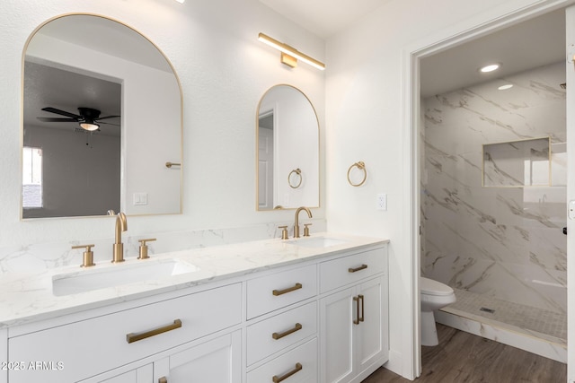 bathroom with ceiling fan, hardwood / wood-style floors, tiled shower, vanity, and toilet