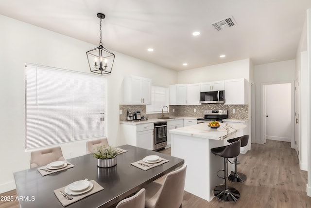 kitchen with sink, appliances with stainless steel finishes, white cabinetry, hanging light fixtures, and a center island