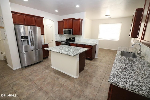 kitchen with appliances with stainless steel finishes, sink, decorative backsplash, a center island, and light stone counters