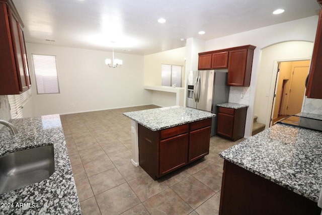 kitchen with a kitchen island, sink, stainless steel fridge, hanging light fixtures, and light stone countertops