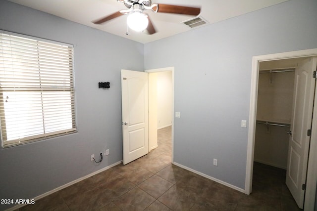 unfurnished bedroom with dark tile patterned floors, a walk in closet, ceiling fan, and a closet