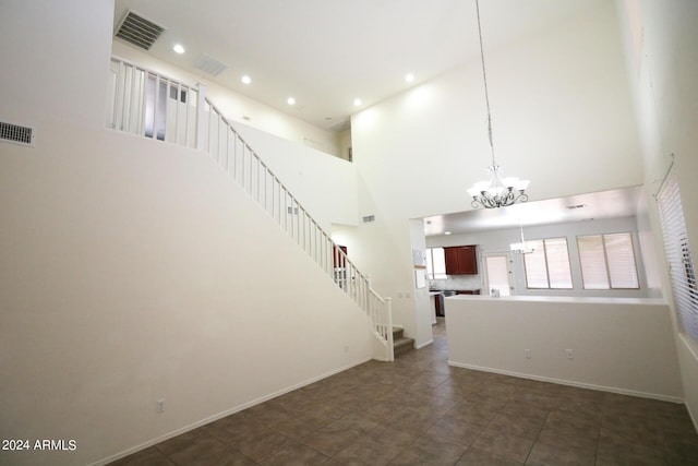 unfurnished living room featuring an inviting chandelier, dark tile patterned flooring, and a high ceiling