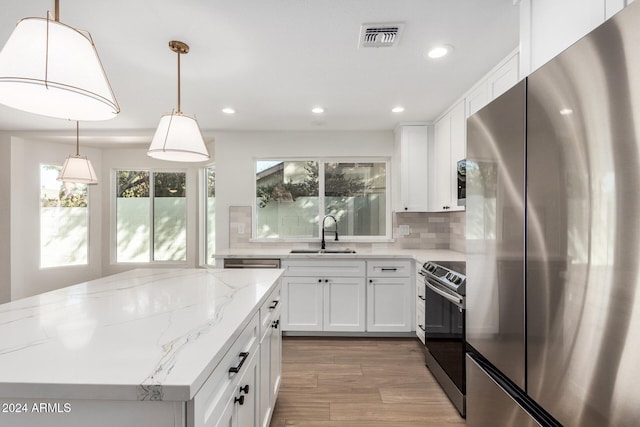 kitchen with white cabinetry, sink, stainless steel appliances, pendant lighting, and light hardwood / wood-style floors