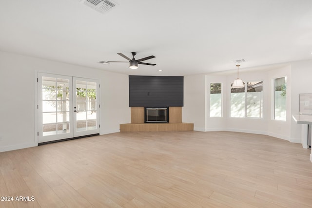 unfurnished living room featuring ceiling fan, a large fireplace, french doors, and light wood-type flooring