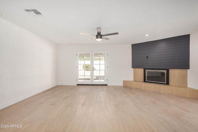 unfurnished living room with a fireplace, french doors, light hardwood / wood-style flooring, and ceiling fan