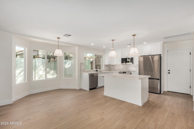 kitchen with pendant lighting, a kitchen island, stainless steel appliances, and light wood-type flooring