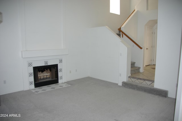 unfurnished living room with a tile fireplace, a high ceiling, and light colored carpet