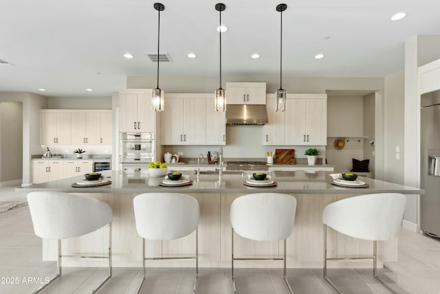 kitchen with double oven, a large island with sink, sink, and pendant lighting