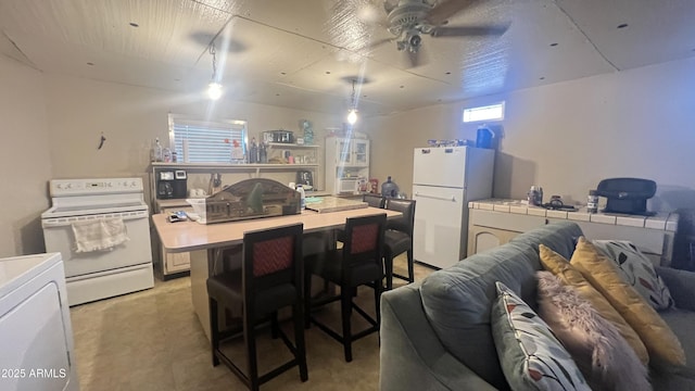 kitchen featuring a breakfast bar, washer / dryer, a center island, ceiling fan, and white appliances