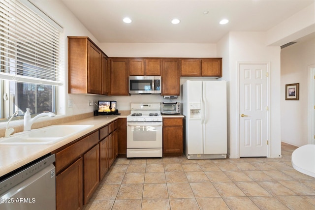 kitchen with brown cabinetry, appliances with stainless steel finishes, light countertops, a sink, and recessed lighting