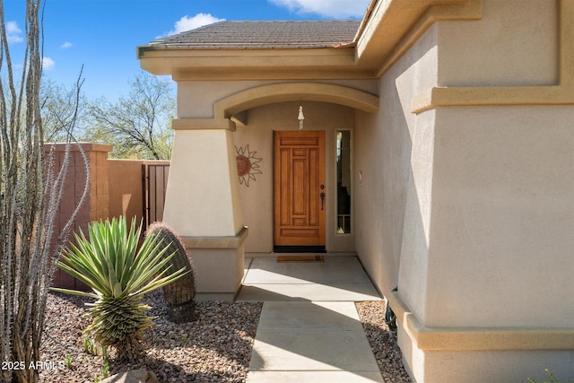 doorway to property featuring roof with shingles, fence, and stucco siding