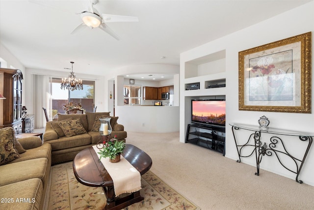 carpeted living area featuring ceiling fan with notable chandelier and a lit fireplace