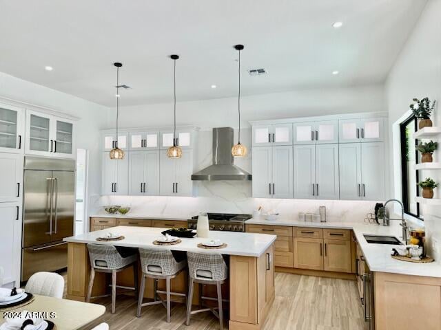 kitchen with hanging light fixtures, a kitchen island, sink, wall chimney exhaust hood, and stainless steel appliances