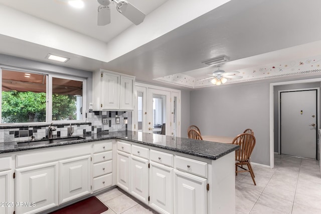 kitchen featuring a raised ceiling, white cabinetry, ceiling fan, a sink, and a peninsula