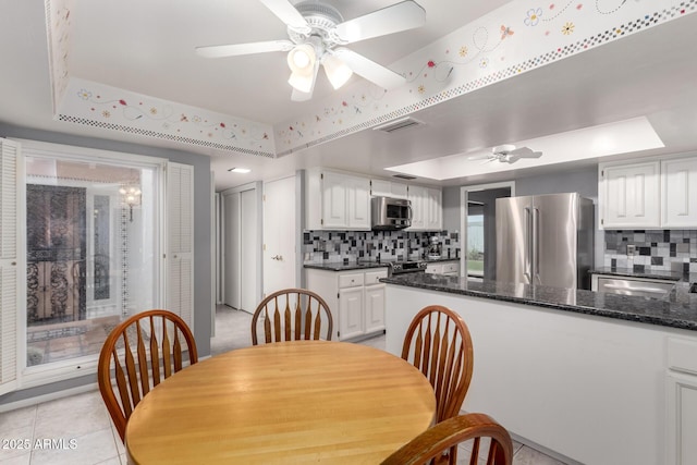 dining room with light tile patterned floors, a tray ceiling, visible vents, and a ceiling fan