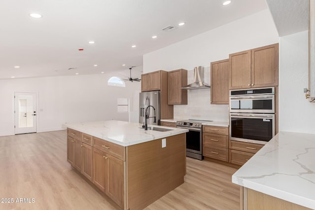 5736 E Singletree St, Apache Junction, AZ 85119 - kitchen with stainless steel appliances, wall chimney exhaust hood, light wood finished floors, a center island with sink, and ceiling fan