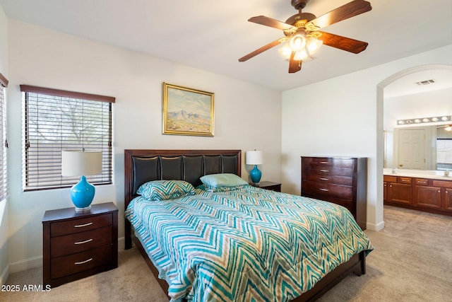 bedroom with ceiling fan, light colored carpet, and connected bathroom